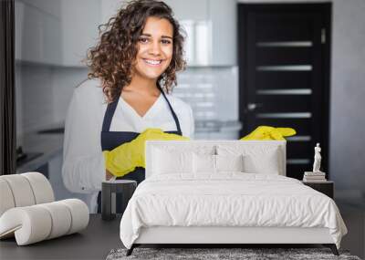 Pretty young latin cleaning lady pointing fingers at blank white board with kitchen in background Wall mural